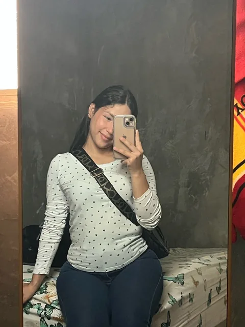 Woman in a white sweater taking a mirror selfie in her bedroom
