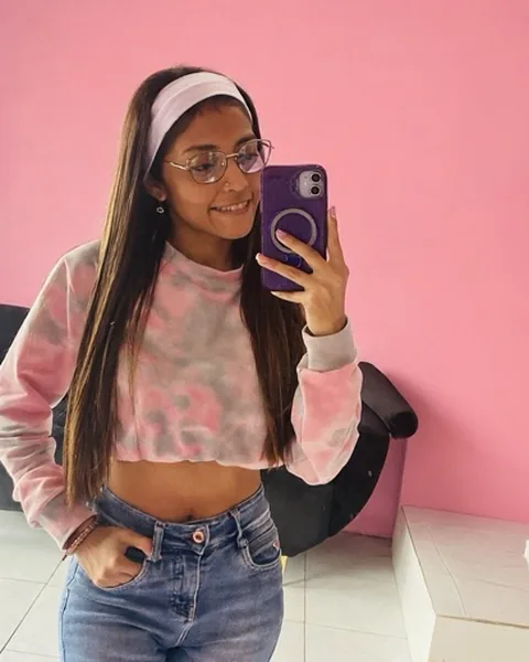 Woman in a pink sweater taking a mirror selfie against a pink wall